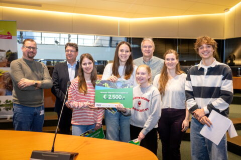 Groep mensen presenteert een cheque van €2500 voor het winnen van een schoolpleinenprijs.