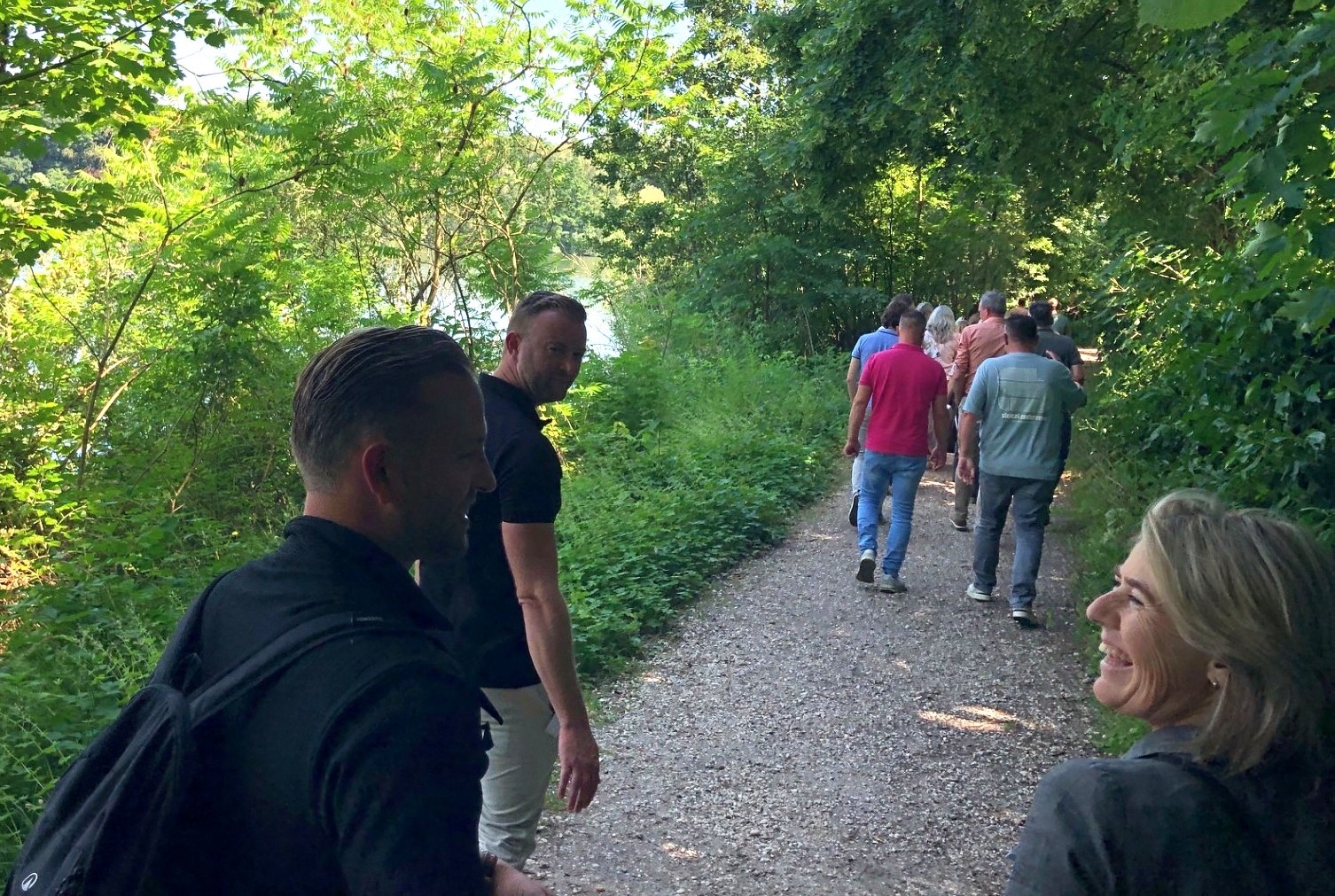 Een groep mensen wandelt op een bosrijk pad op een zonnige dag.