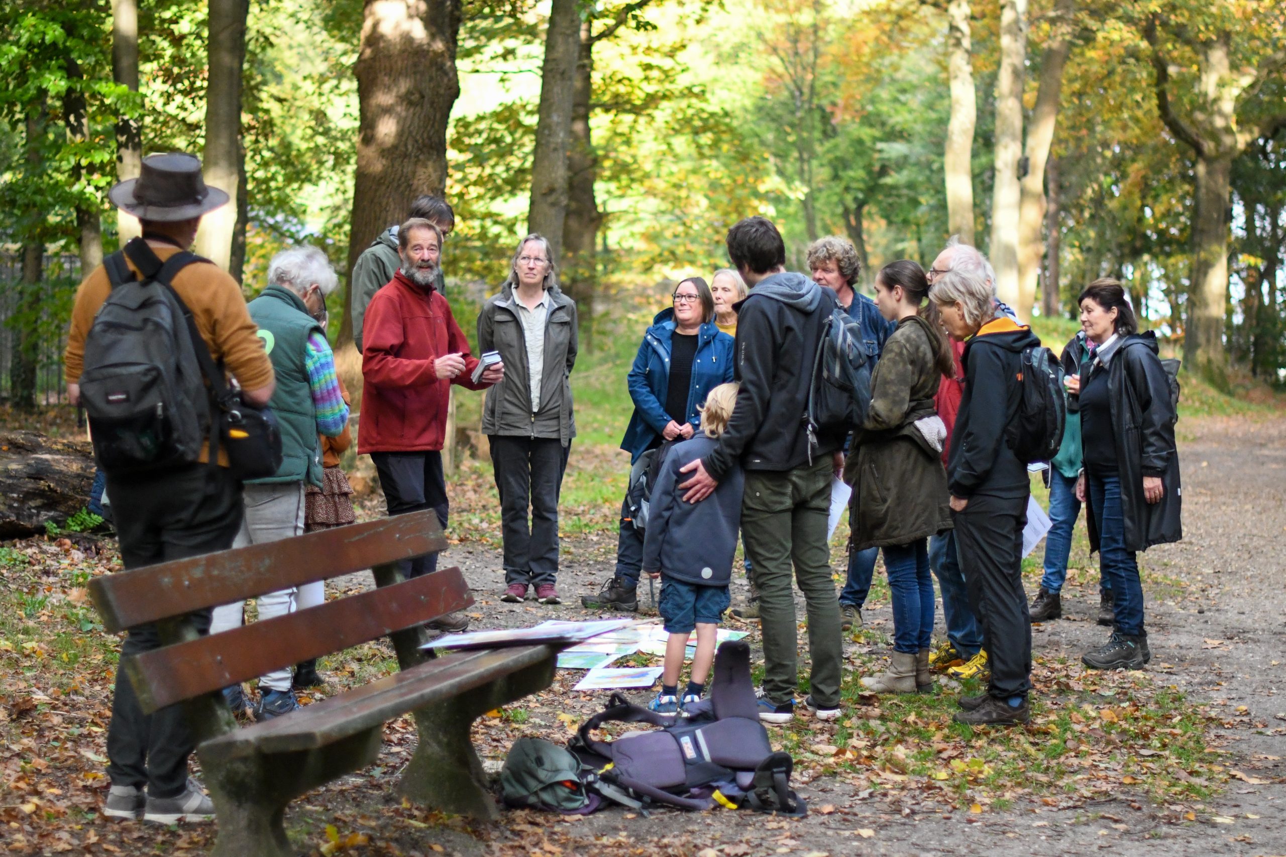Een groep mensen verzameld in een bos, luisterend naar een man die iets uitlegt.
