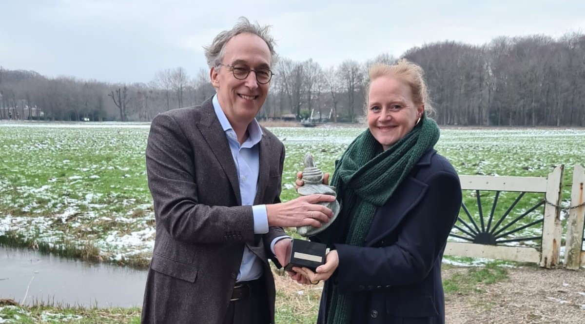 Twee mensen houden samen een stenen beeldje vast in een besneeuwd weiland.