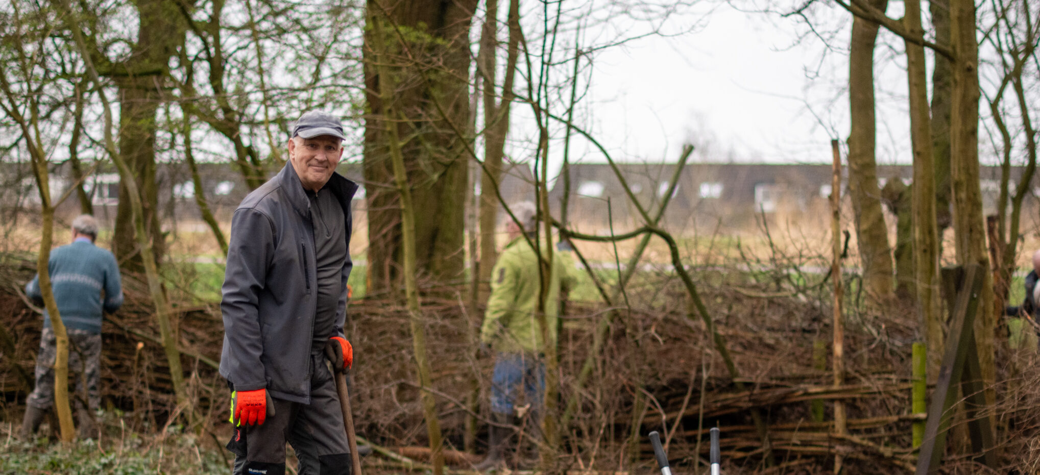 Man met rode handschoenen werkt buiten in een bosrijk gebied, omringd door takken en bomen.