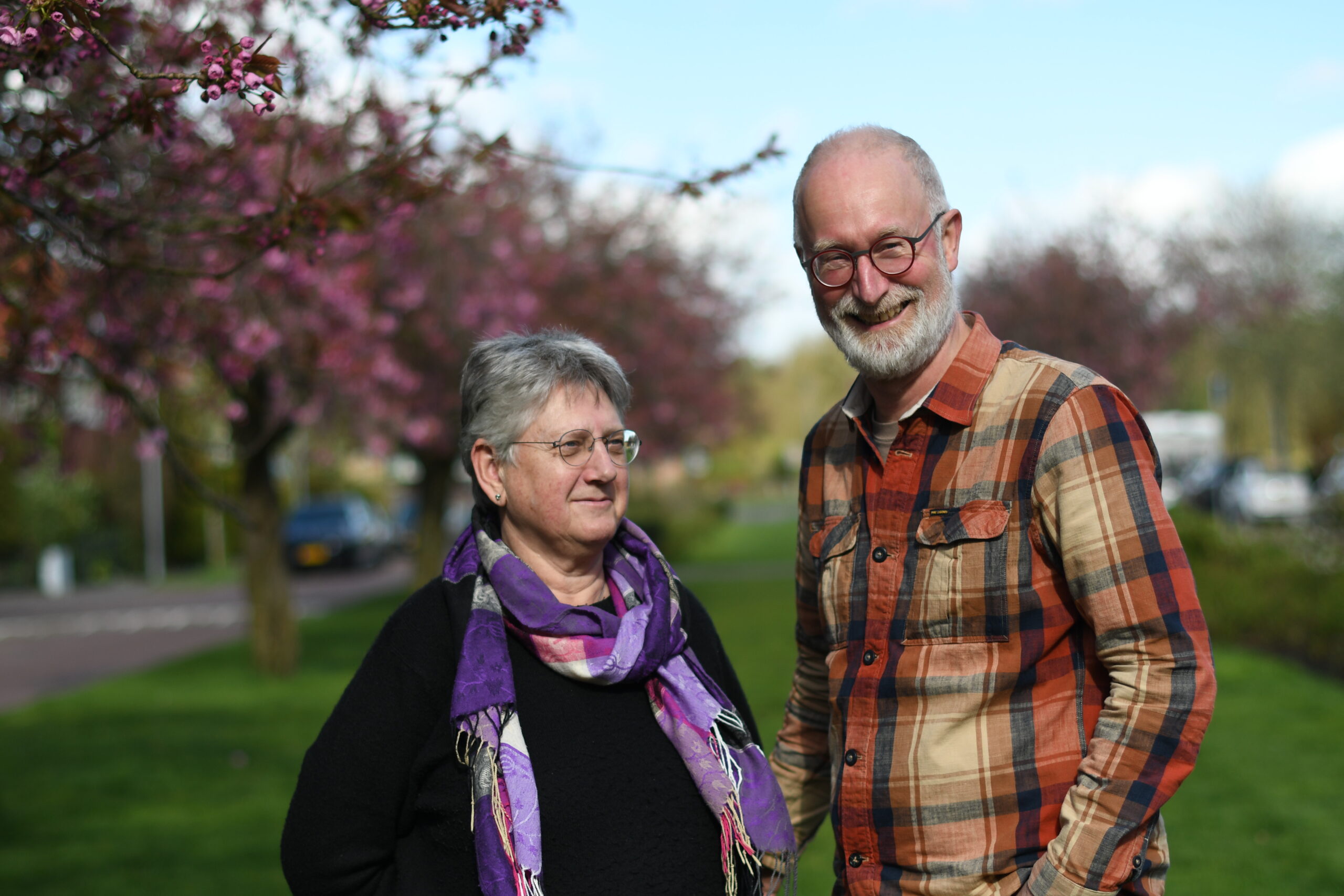 Een lachend stel buiten bij bloeiende paarse bomen.