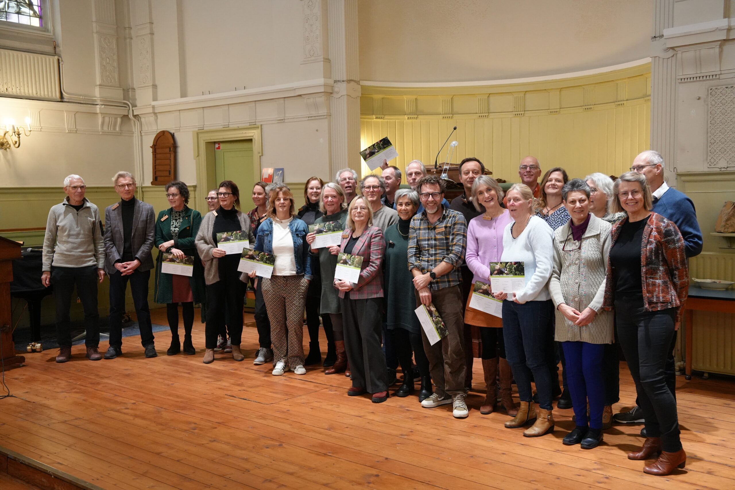 Groep mensen poseert met certificaten in een ruime, goed verlichte zaal.
