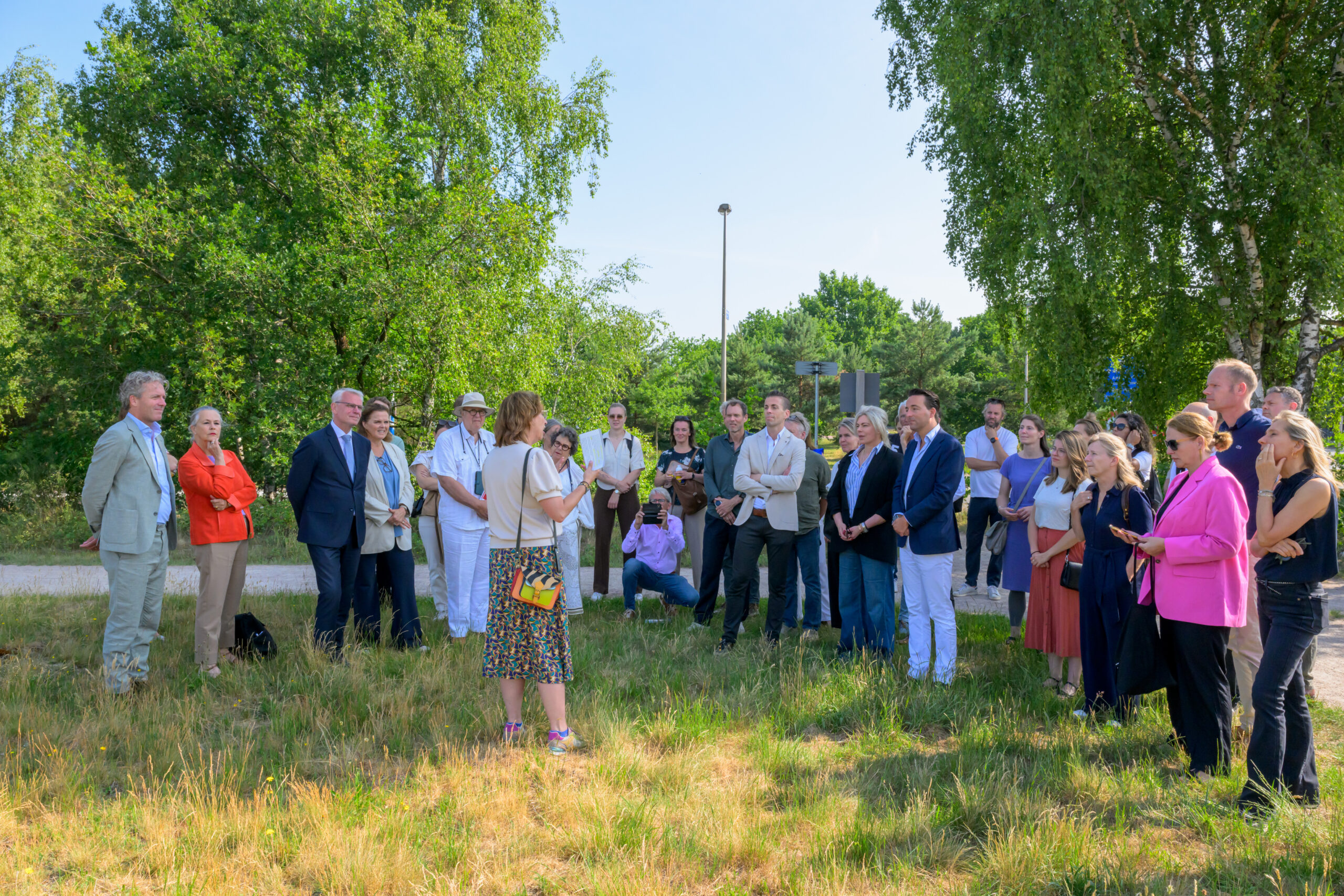 Een groep mensen luistert naar een spreker in een groene, buitenomgeving.