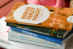 Stapeltje boeken met bovenop "Werken vanuit kracht" op een houten tafel.