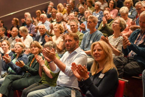 Een zaal vol mensen klapt enthousiast tijdens een event.