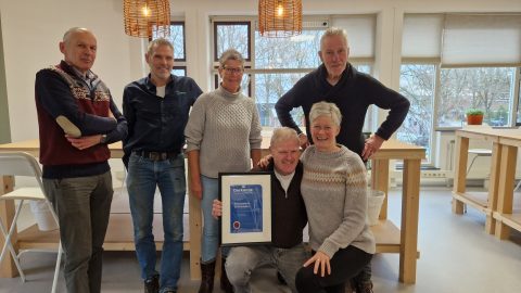 Groep mensen poseert met een oorkonde in een lichte, moderne ruimte.