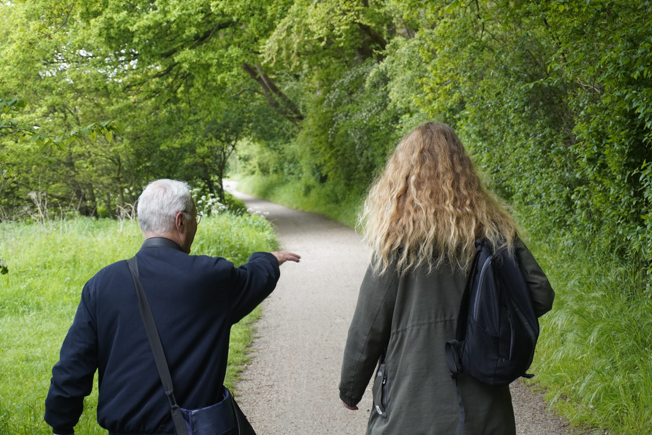 Twee mensen wandelen op een groen bospad, één wijst iets aan.