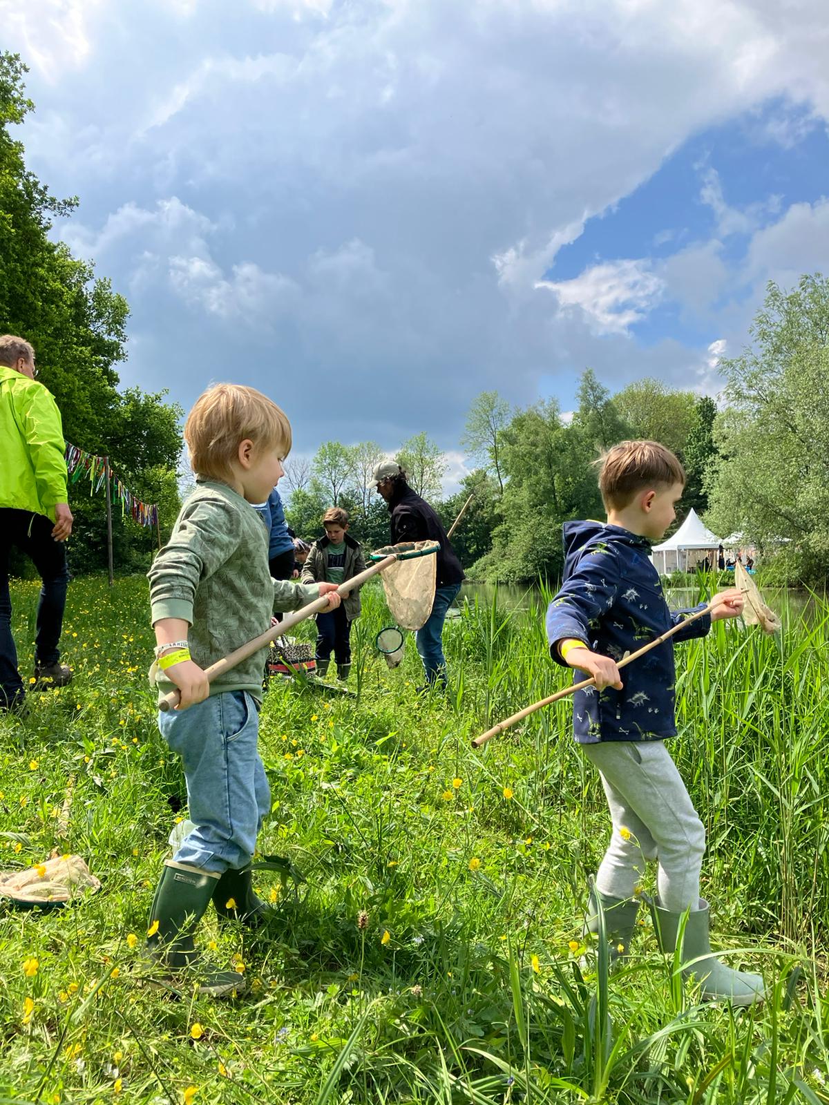 Twee jonge kinderen vangen insecten met netten in een zonnig grasveld met bloemen.