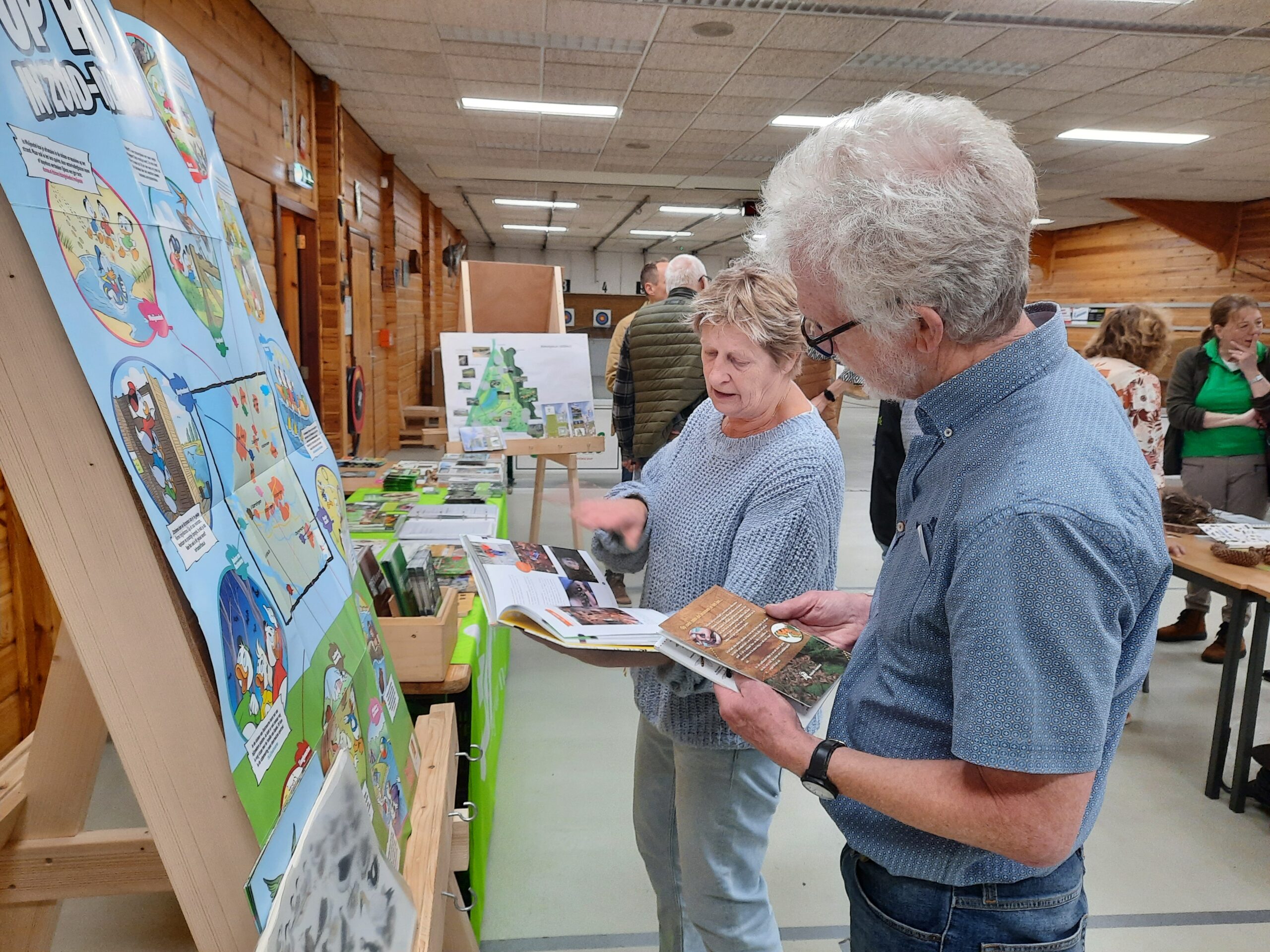 Twee mensen bekijken educatieve panelen en brochures in een tentoonstellingsruimte.