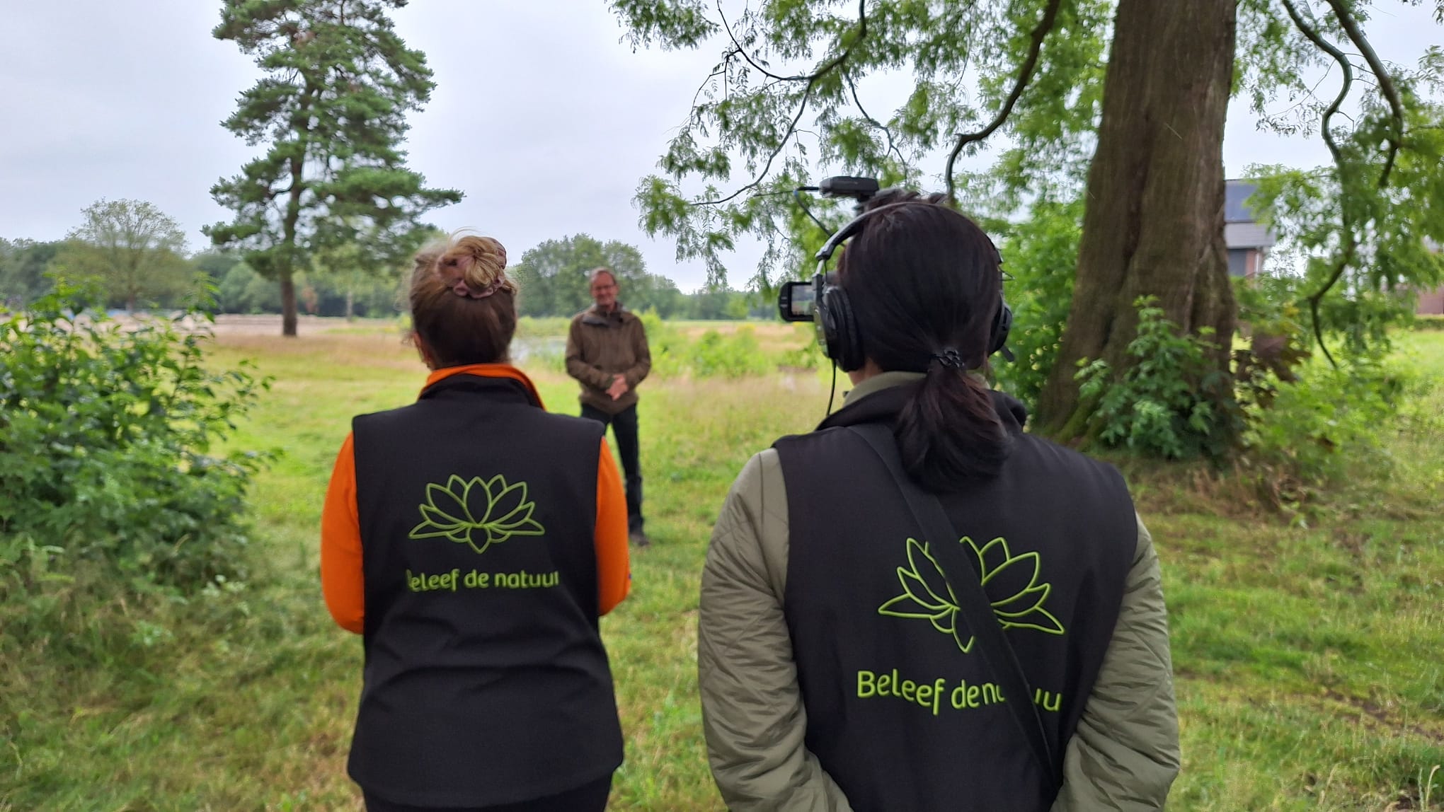 Twee mensen filmen een natuurpresentatie in een groen, bosrijk gebied.