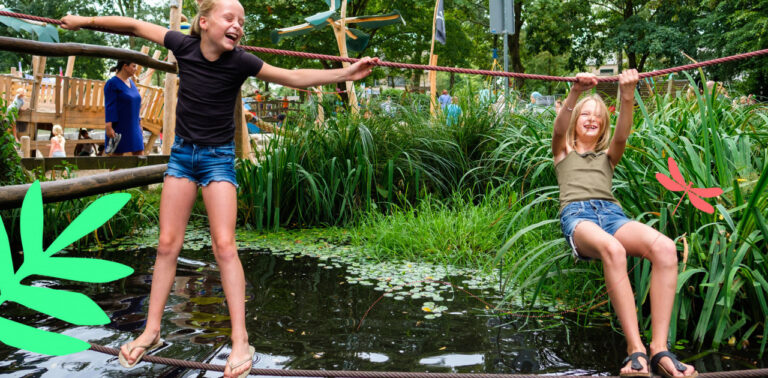Twee lachende meisjes balanceren op een touw boven een vijver in een speeltuin.