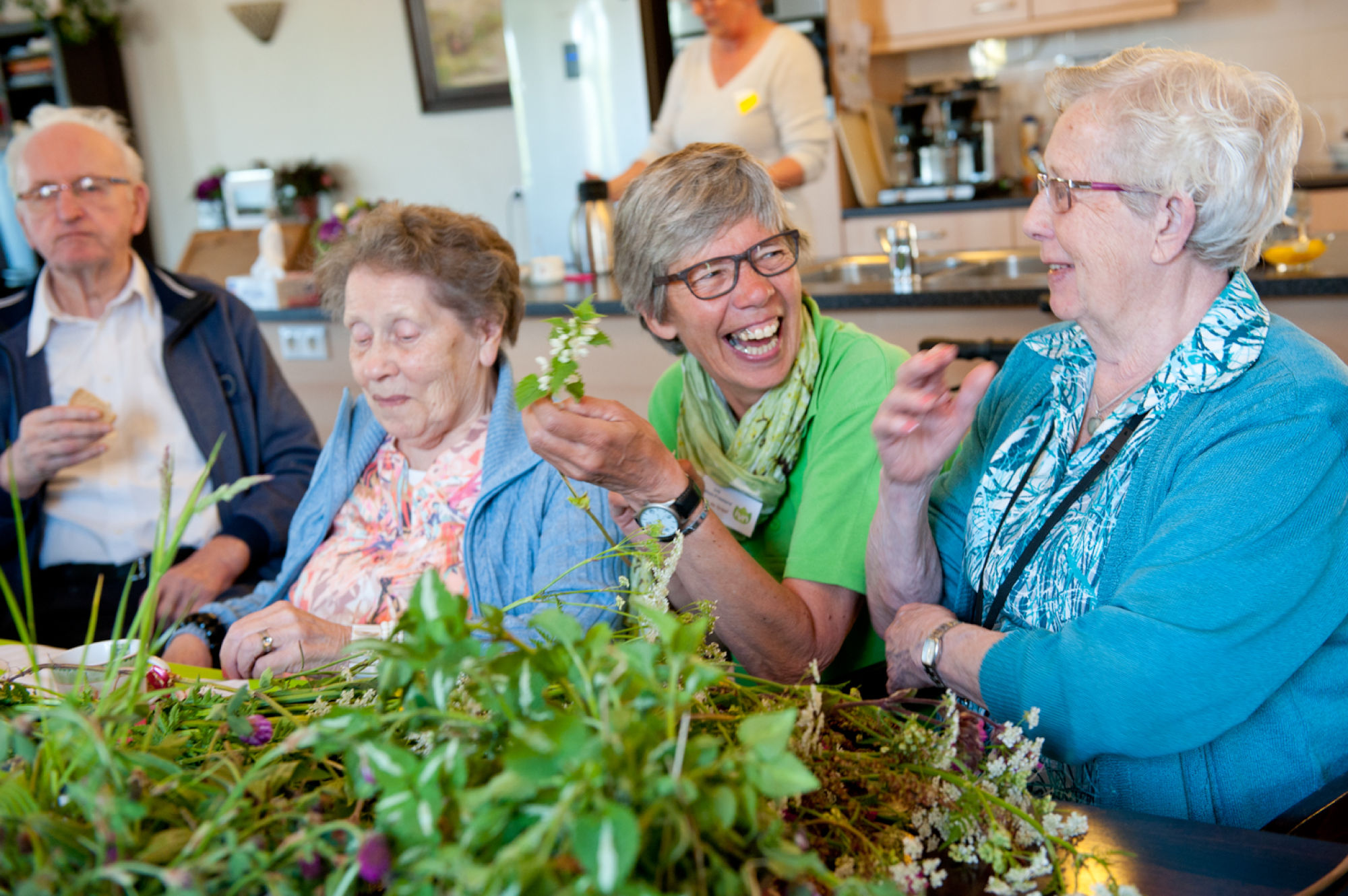 Een groep ouderen lacht en bekijkt planten aan tafel.