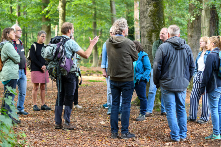 Groep mensen luistert naar een gids in een bosrijke omgeving.