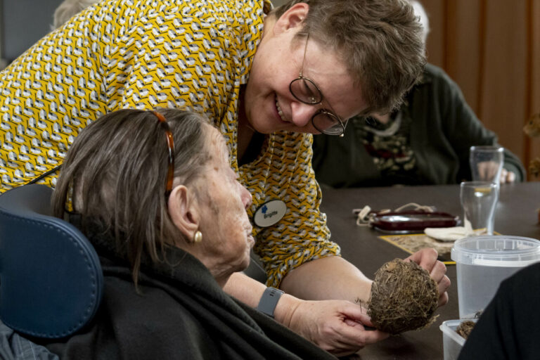Twee mensen interacteren, waarvan één een bruine bol vasthoudt aan een tafel met glazen.