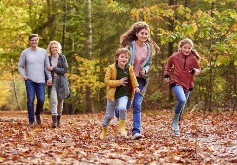 Gezin wandelt en rent door een herfstbos, omgeven door felgekleurde blaadjes.