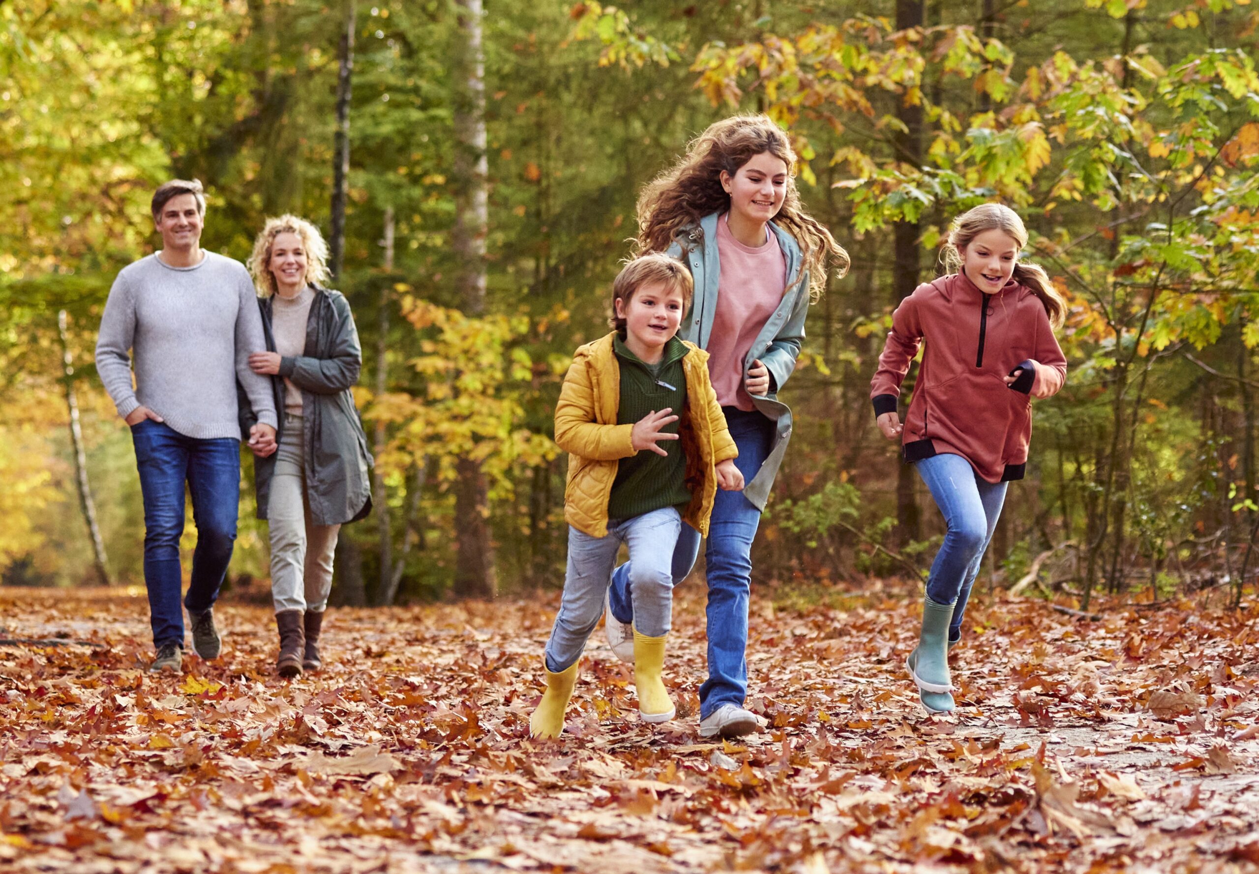 Gezin wandelt en rent door een herfstbos, omgeven door felgekleurde blaadjes.