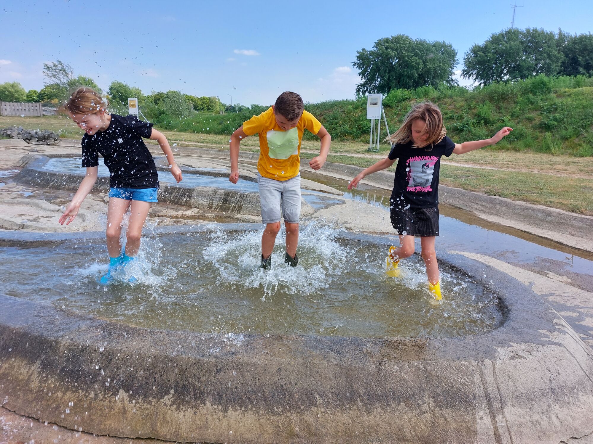 Drie kinderen spelen en spetteren in ondiep water op een zonnige dag in een park.