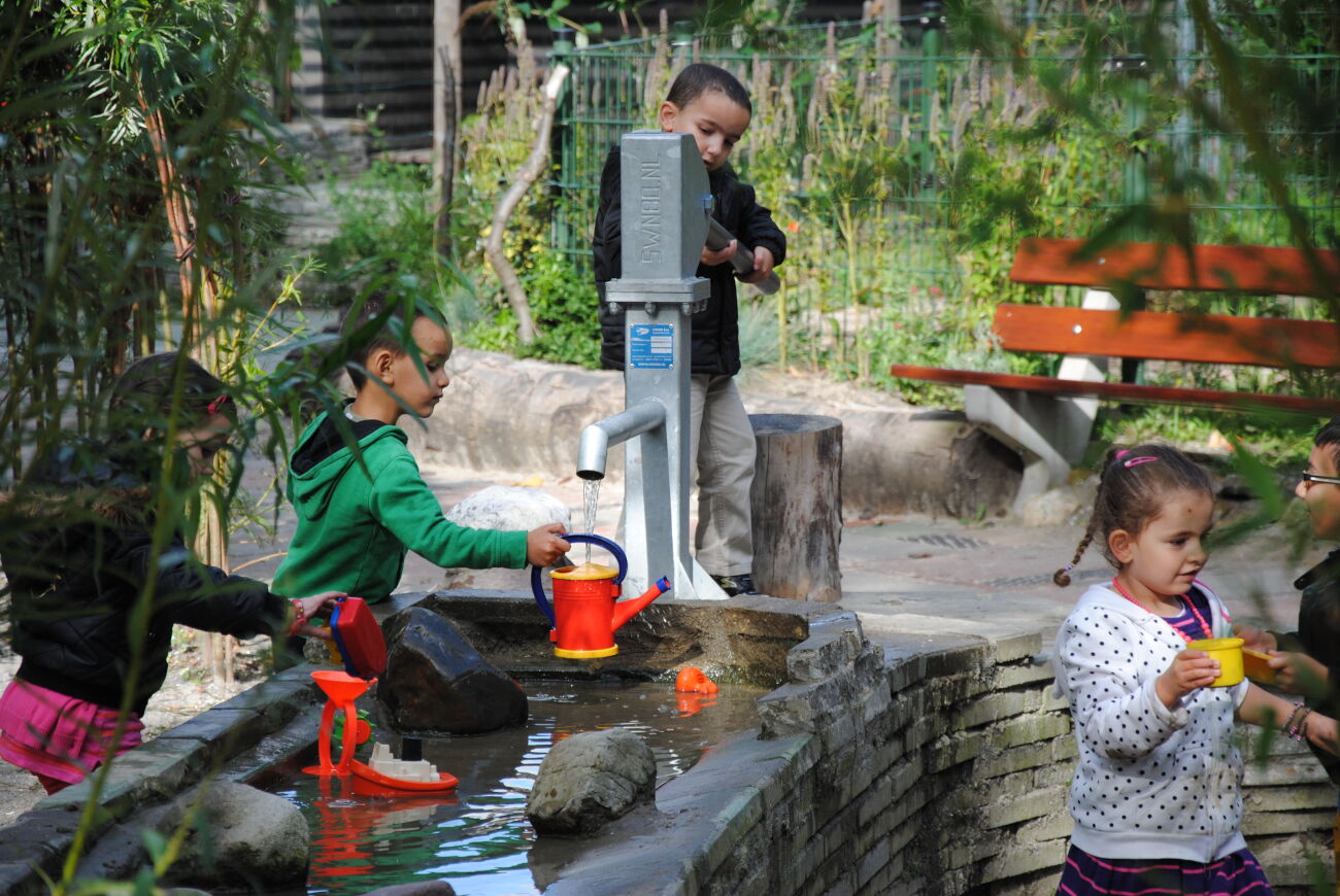 Kinderen spelen in een tuin met waterpompen en gieters.