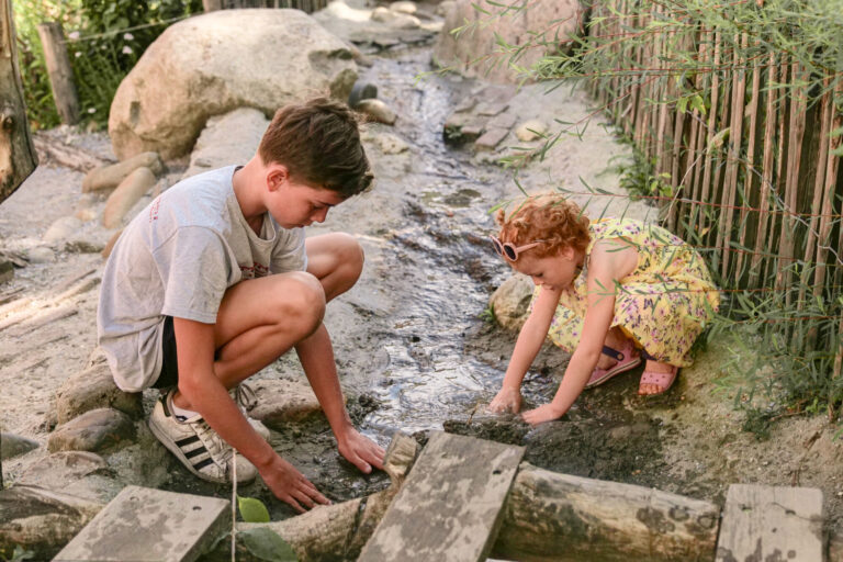 Twee kinderen spelen met water in een natuurlijke buitenspeeltuin.