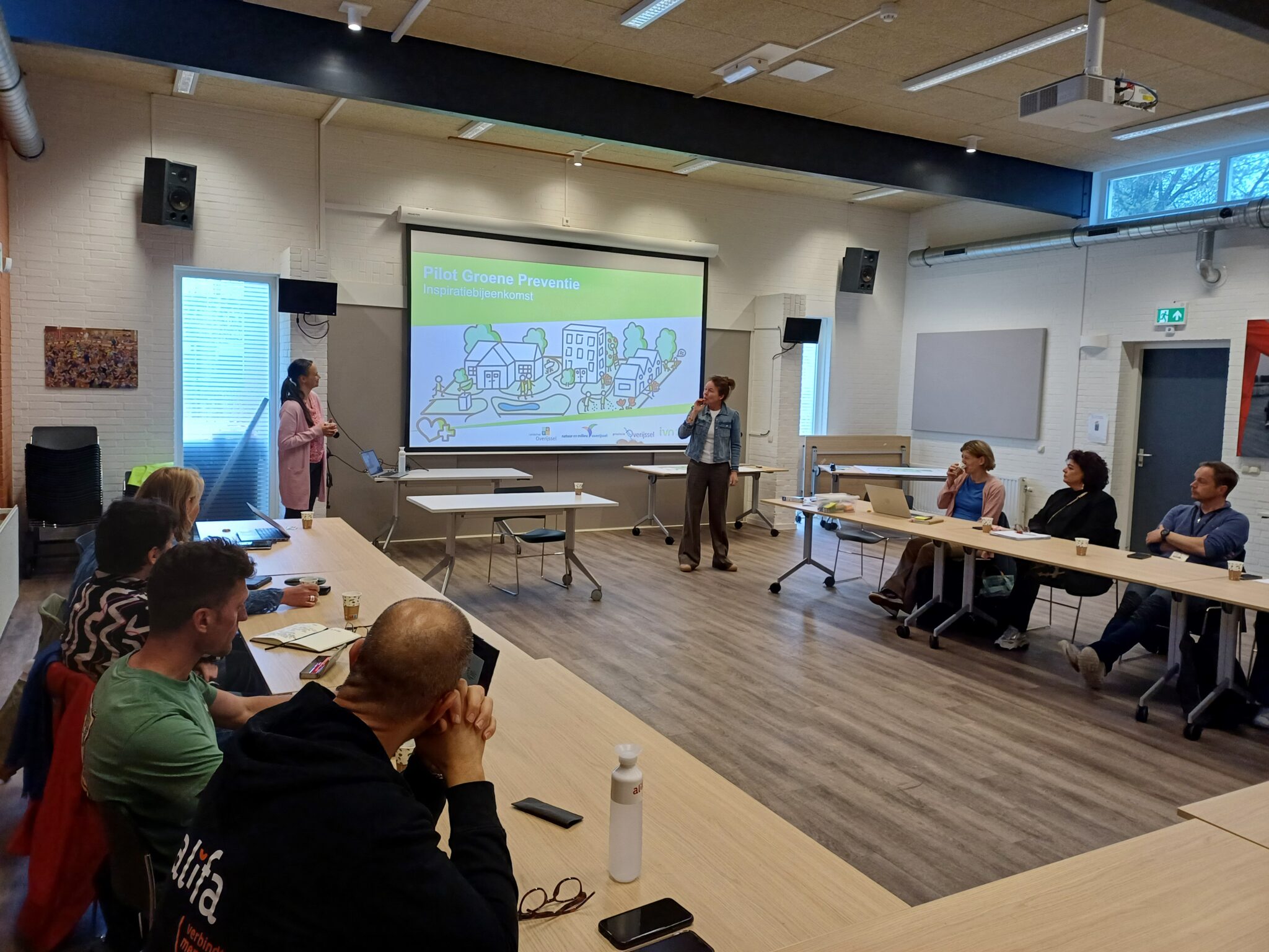 Een presentatie over "Pilot Groene Preventie" in een vergaderruimte met deelnemers.