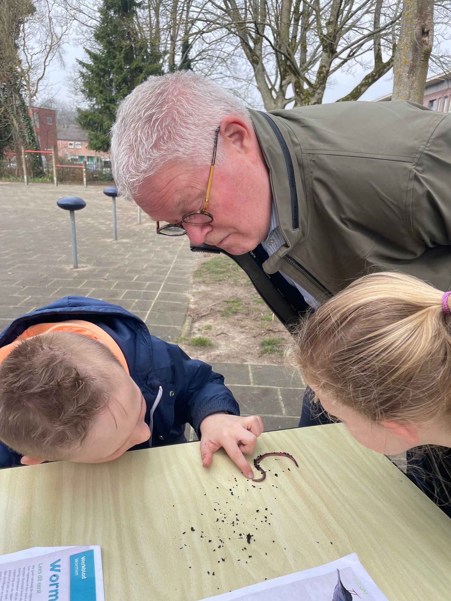Drie mensen bestuderen een worm op een tafel buiten.
