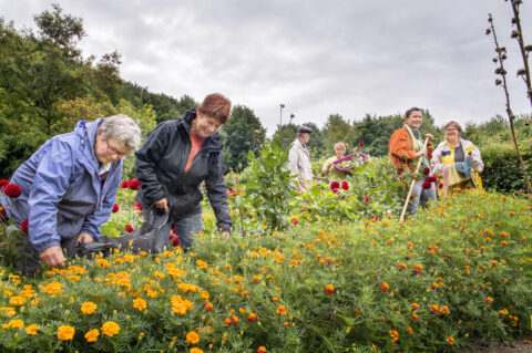 Mensen werken samen in een kleurrijke bloemen- en groentetuin op een bewolkte dag.