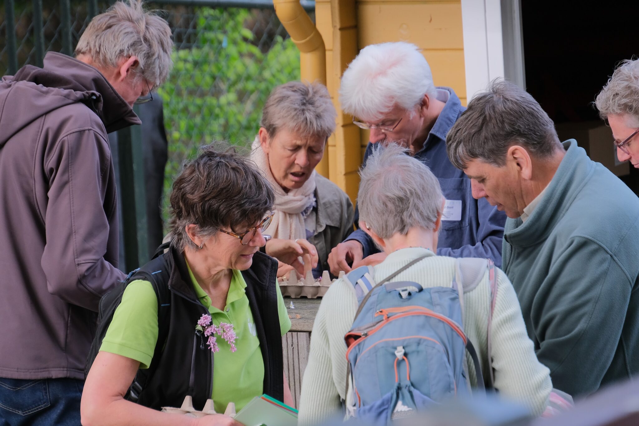 Groep mensen verzameld rond een tafel, kijkend naar een object buiten.