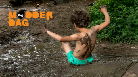 Een kind speelt in de modder tijdens Modderdag, bedekt met modder, omgeven door bos.