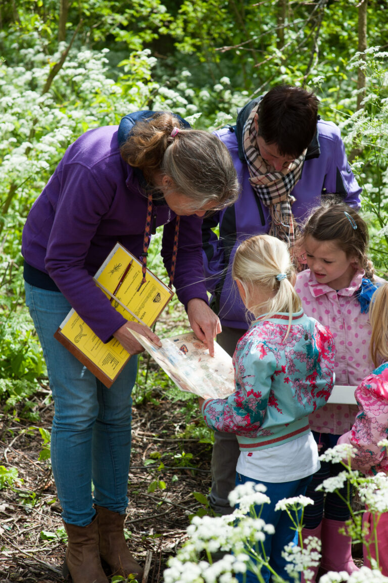Volwassenen en kinderen kijken naar kaarten in een bosrijke omgeving.