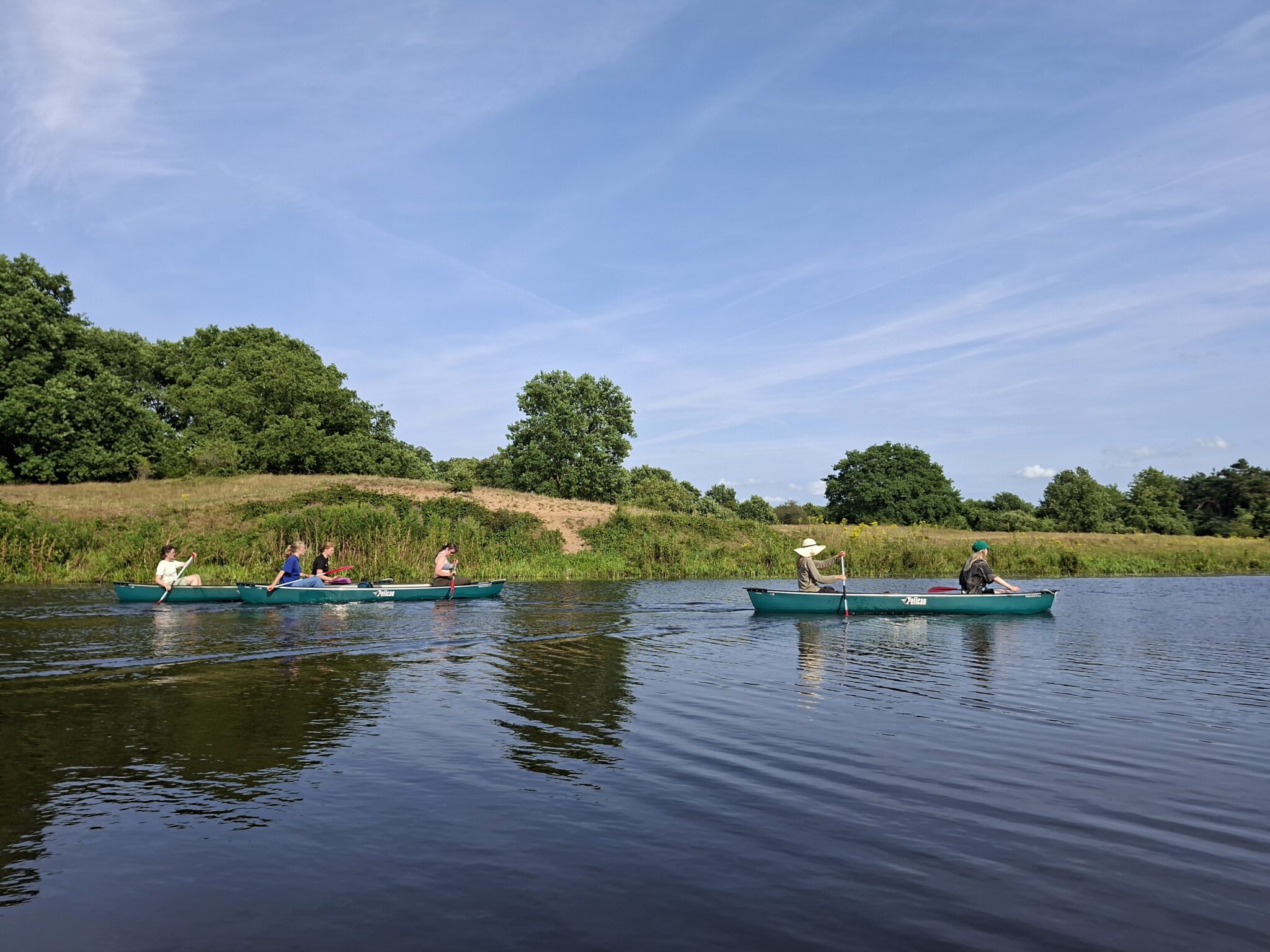 Twee kano's met mensen peddelen op een rustige rivier omringd door groene oevers en blauwe lucht.