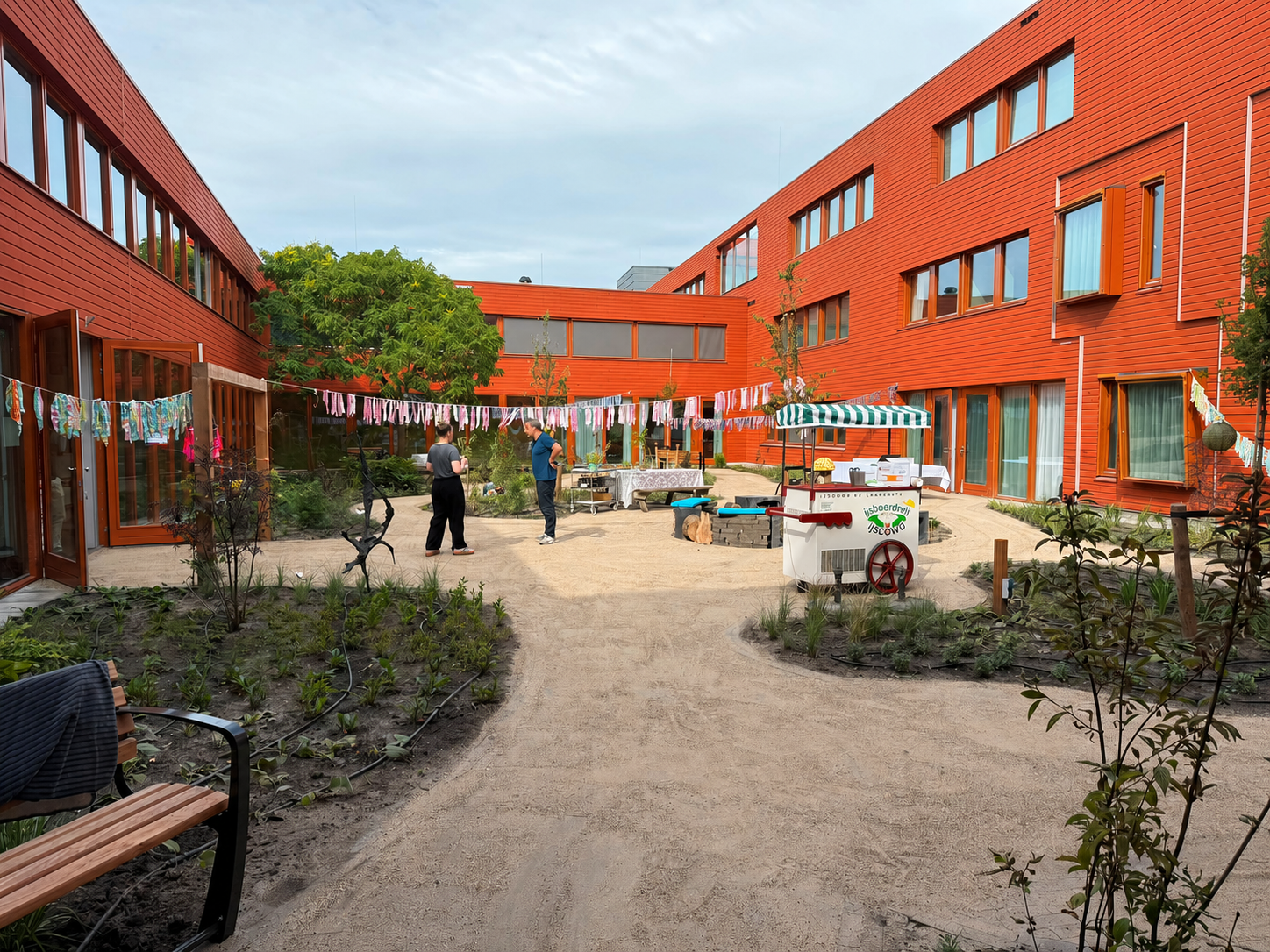 Binnenplaats met rode gebouwen, kleurrijke slingers, mensen en een marktkraam.