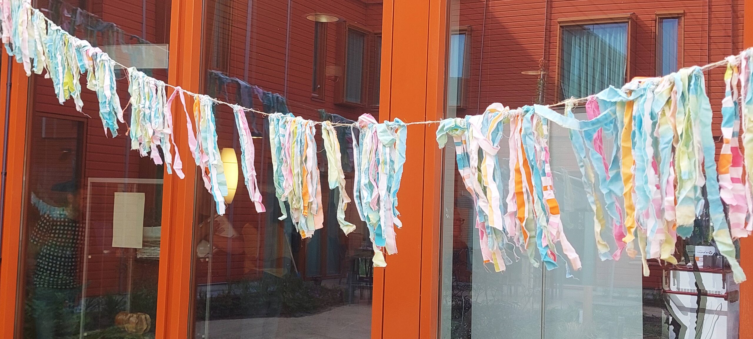 Gekleurde stoffen slingers hangen buiten voor een gebouw met glazen ramen.