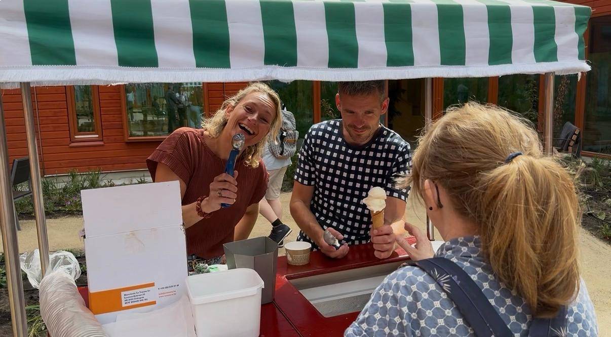Twee mensen serveren ijs onder een groen-wit gestreepte kraam aan een klant.