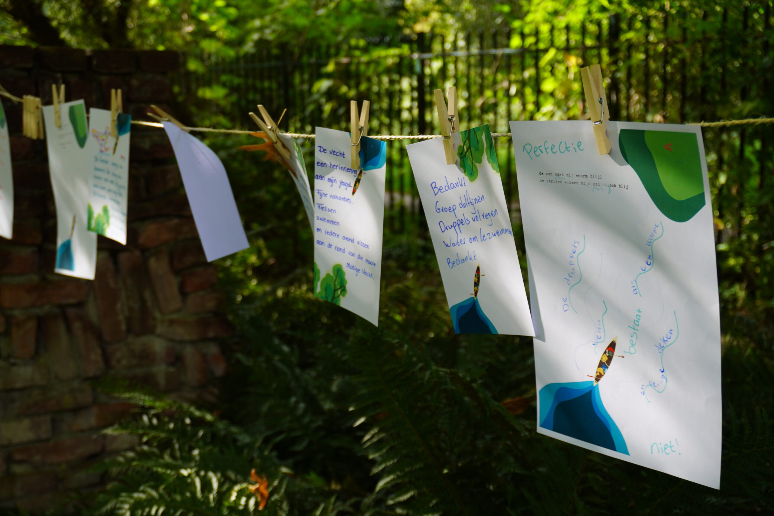 Papieren met handgeschreven teksten hangen aan een lijn met knijpers in een groene tuin.