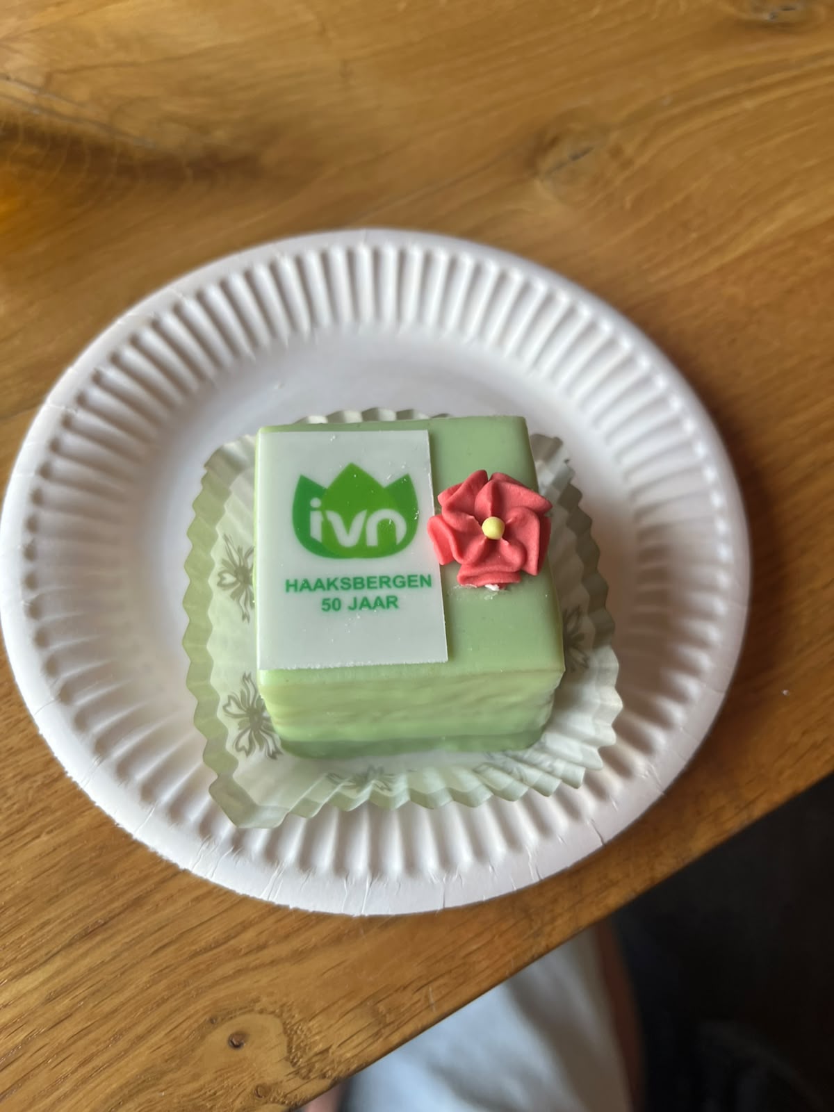Groene taart met "IVN Haaksbergen 50 jaar" en rode bloem, op een papieren bordje.