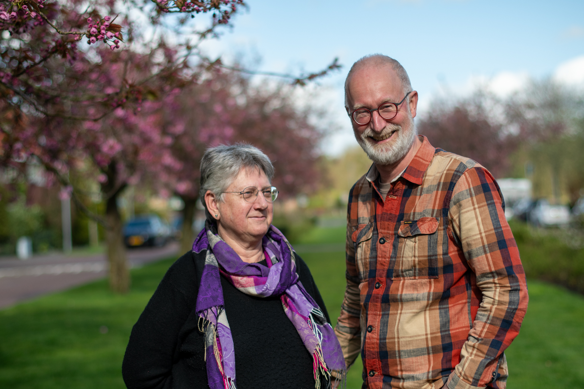 Een glimlachend paar onder bloeiende bomen in een parkachtige omgeving.