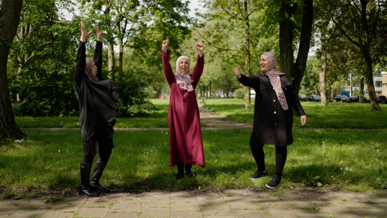 Drie vrouwen in een park, vrolijk hun armen in de lucht stekend.