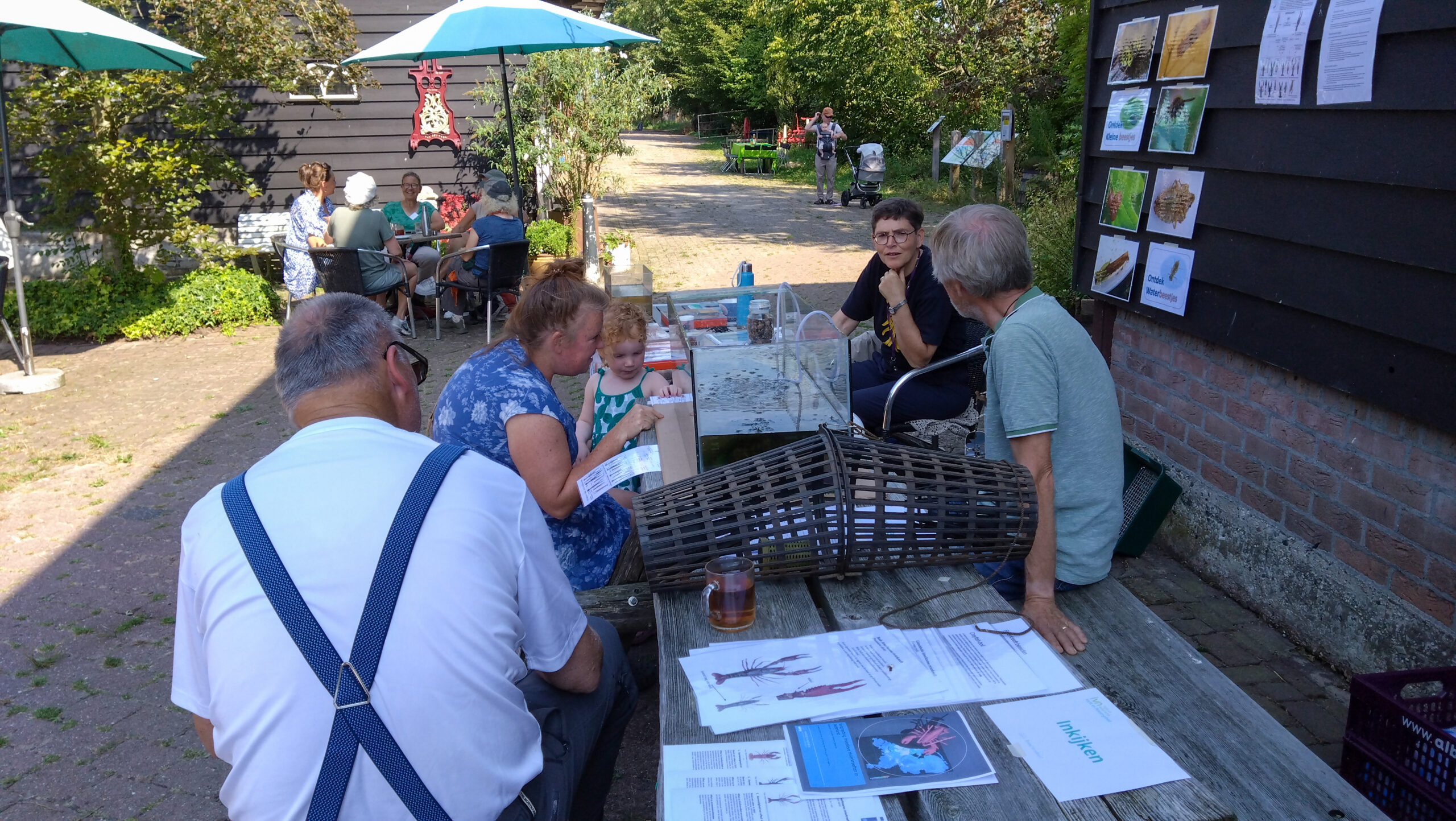 Mensen zitten rond een tafel buiten, omringd door informatieve papieren en een aquarium.