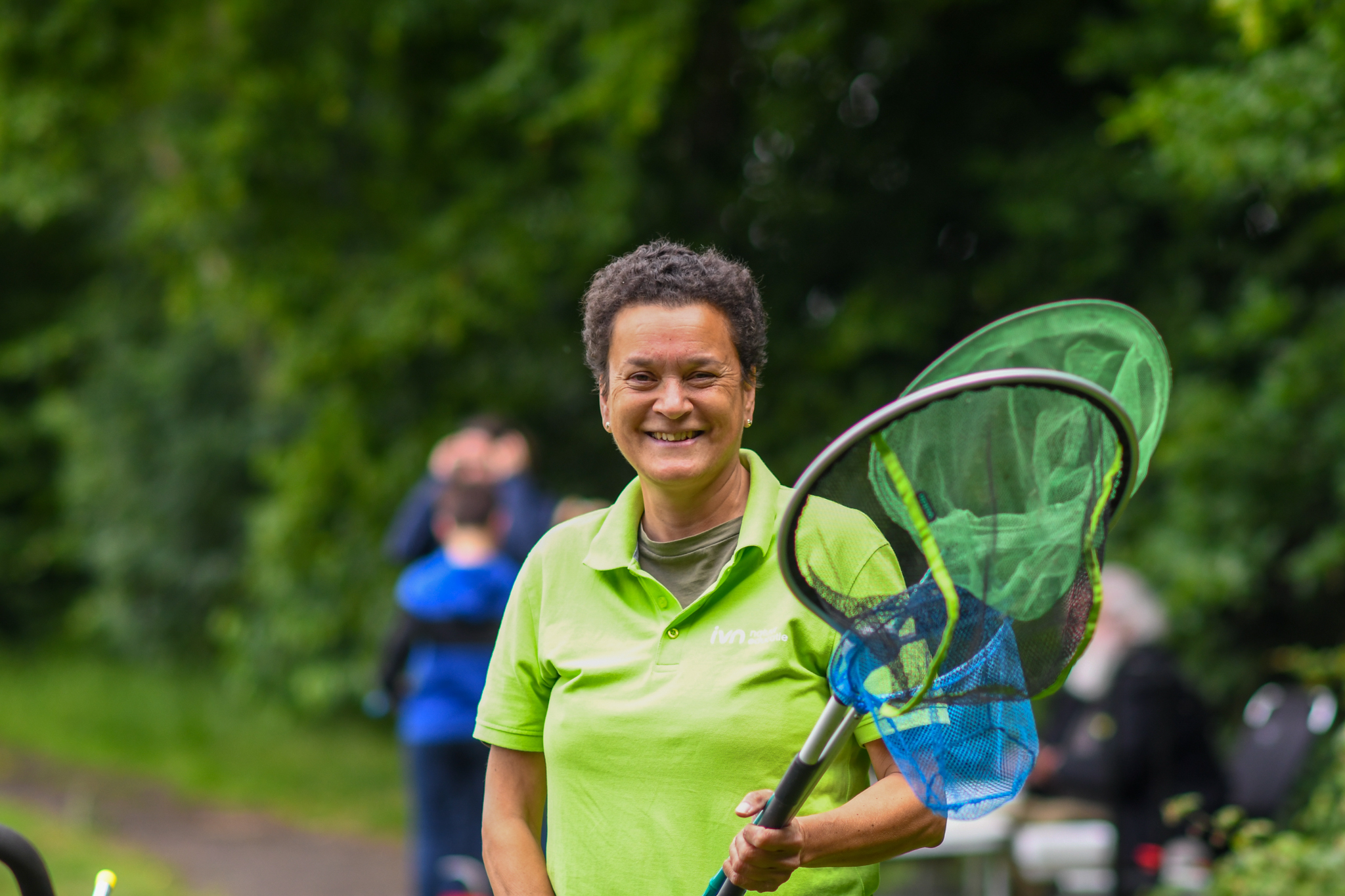 Persoon in groen shirt houdt een schepnet vast, met bomen op de achtergrond.