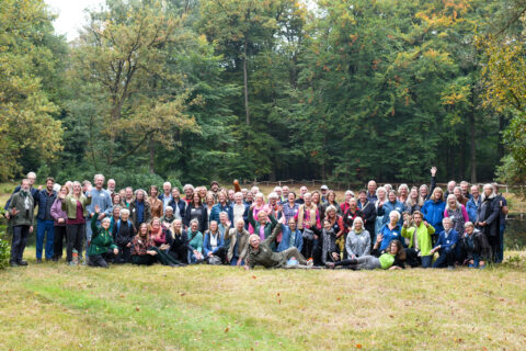 Een grote groep mensen poseert voor een foto in een bosachtige omgeving.