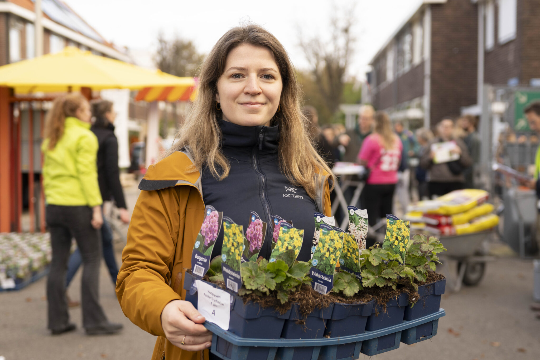 Vrouw met tray vol bloemenplanten op een drukke marktstraat.