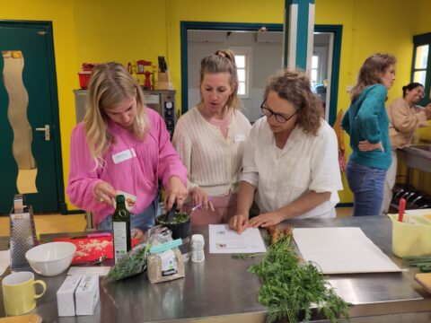 Drie vrouwen bereiden samen een maaltijd in een felgele keuken.
