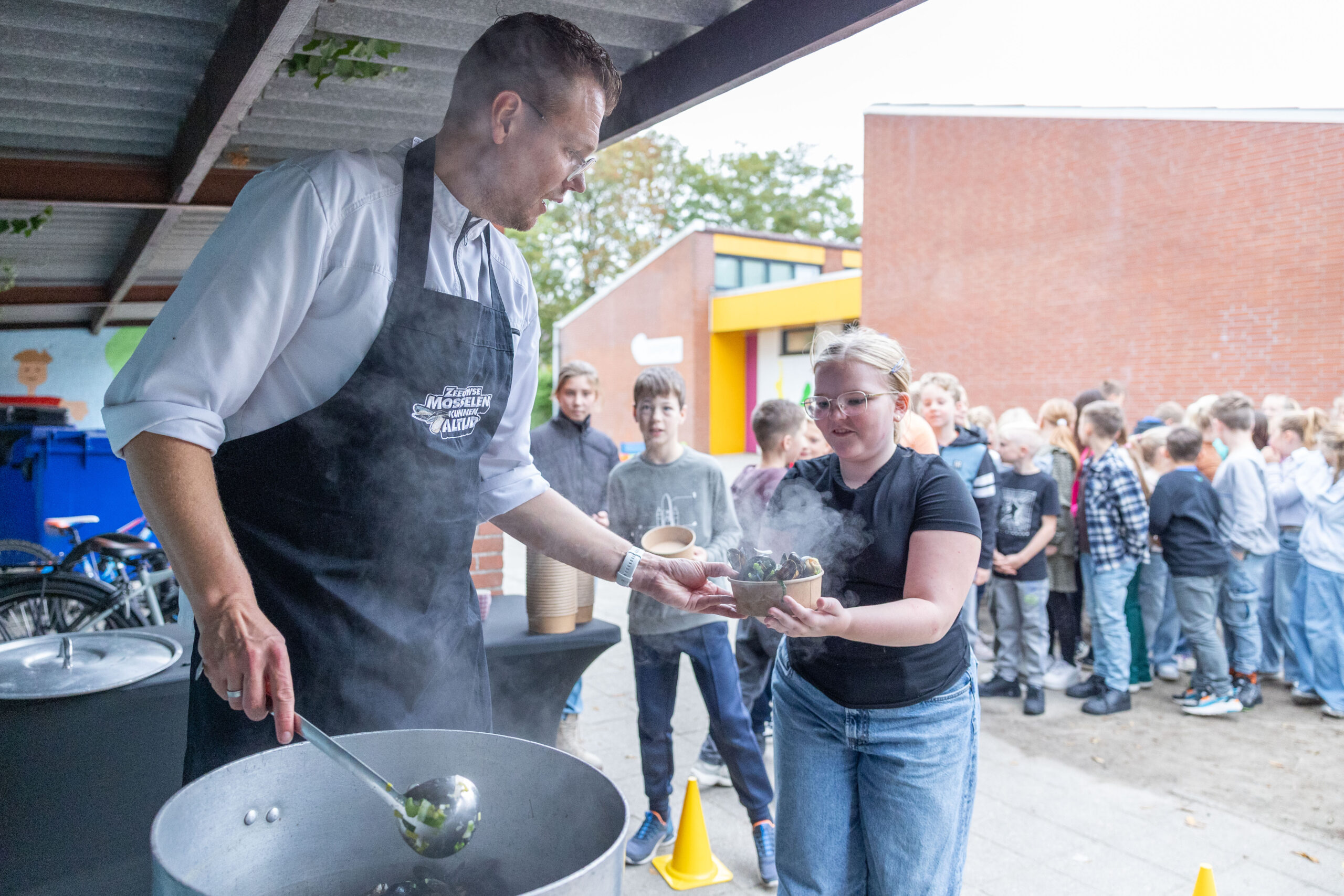 Een kok serveert stoofpot aan een rij kinderen buiten.