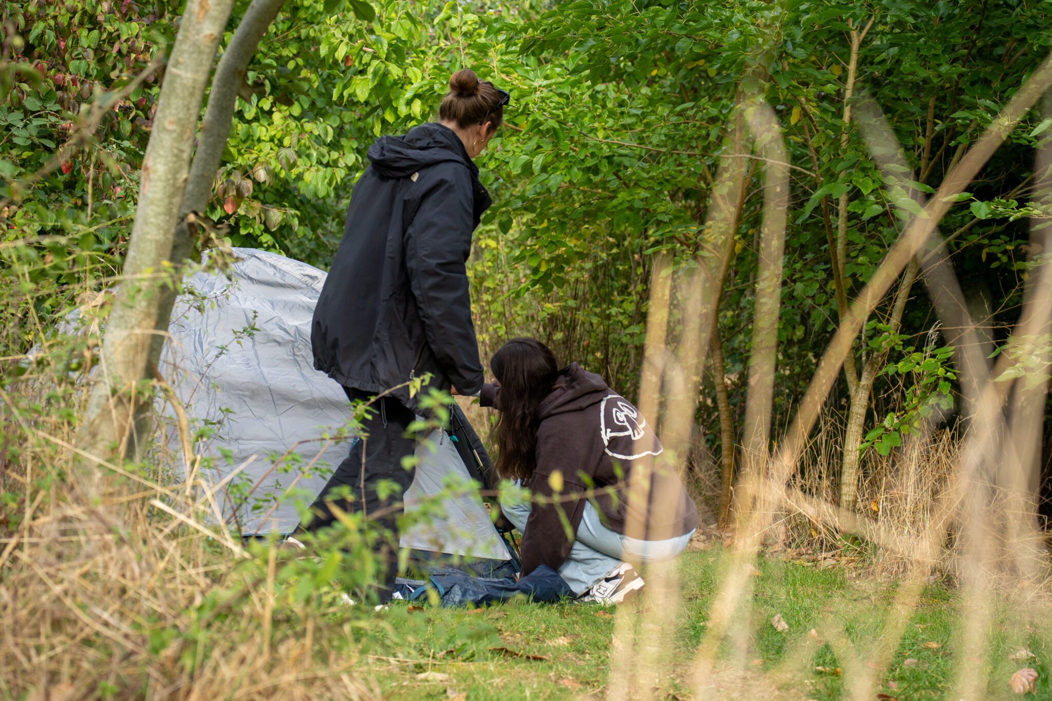 Twee personen zetten een tent op in een bosrijke omgeving.