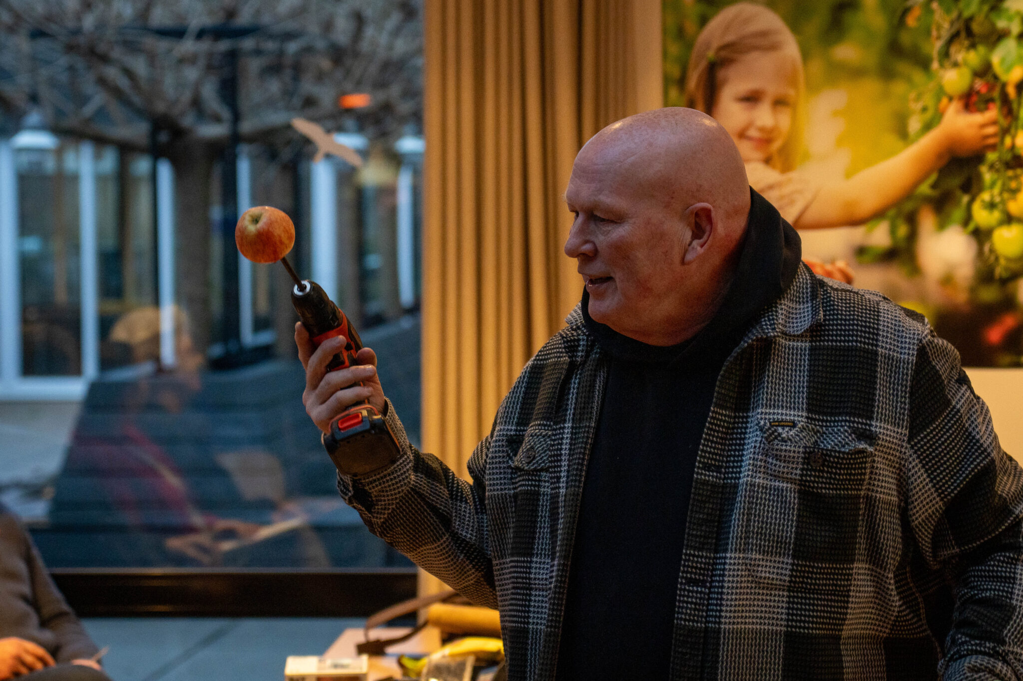 Een man houdt een boormachine vast met een appel erop gespietst in een kamer.