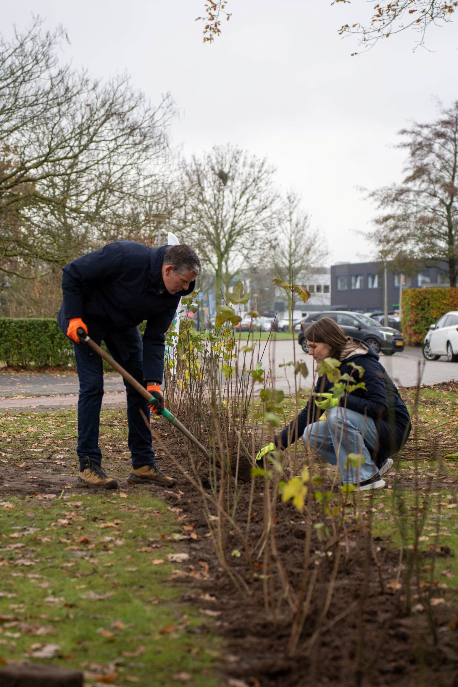 Twee mensen planten struiken langs een straat op een bewolkte dag.