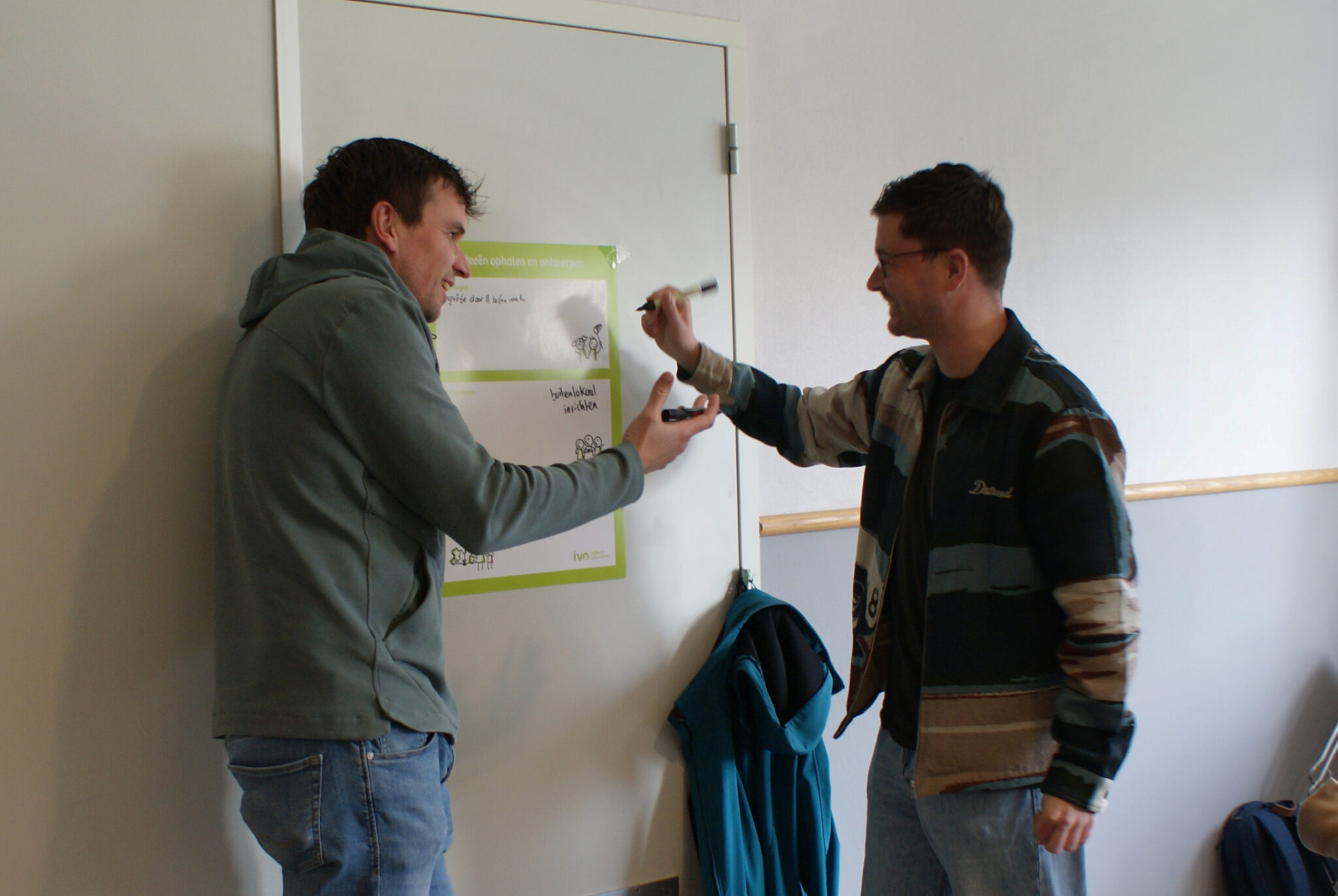 Twee mannen praten en schrijven op een flipover aan een muur.
