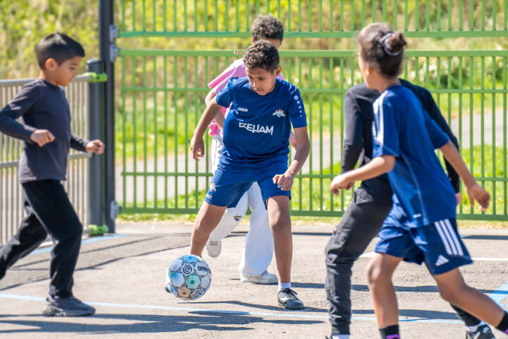 Kinderen spelen voetbal op een zonnige dag op een buitenveldje.