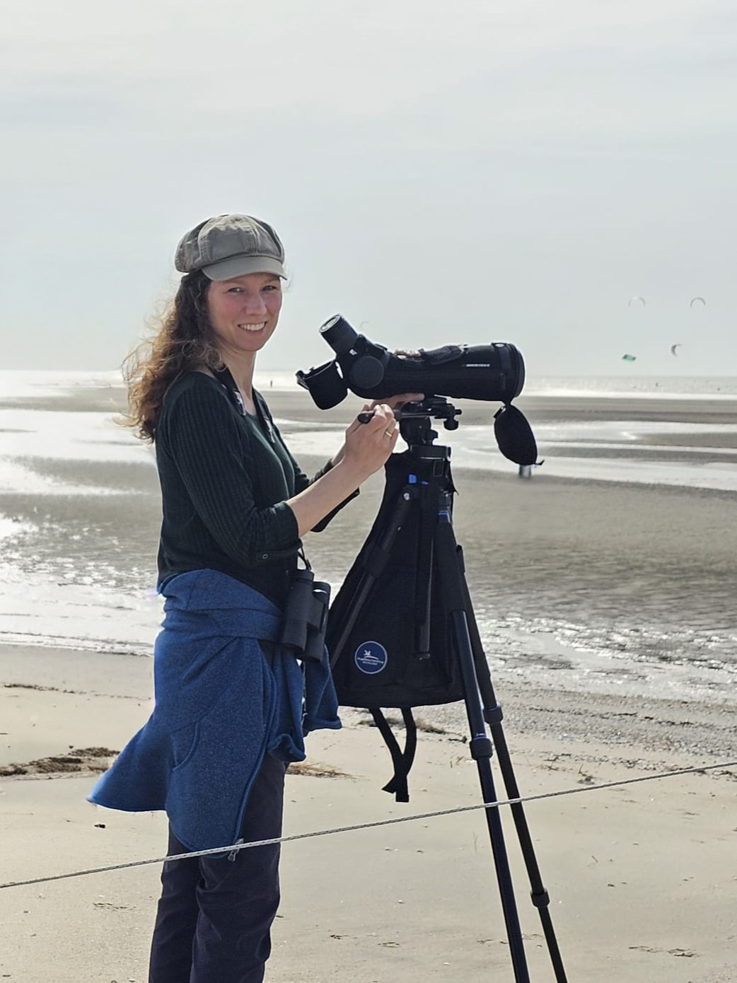 Vrouw observeert het strand met een telescoop op statief.